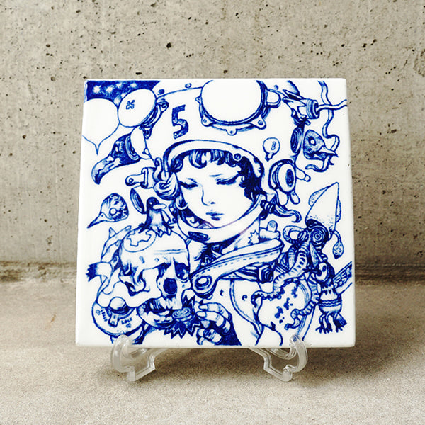 White ceramic square tile with deep blue line art illustration of a woman, looking down wearing a helmet with a "5" on it, surrounded by various skulls and floating bird heads. Tile is propped up on a clear acrylic stand.