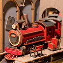 Close up of 3D model kit, displaying an intricate red train pulled up to a platform with a bench and luggage.