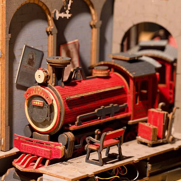 Close up of 3D model kit, displaying an intricate red train pulled up to a platform with a bench and luggage.