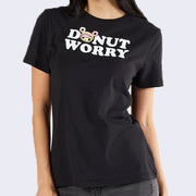 Black t-shirt with "Donut Worry" written in bold white font at top center. Donutella's head stands in for the "O" in donut.