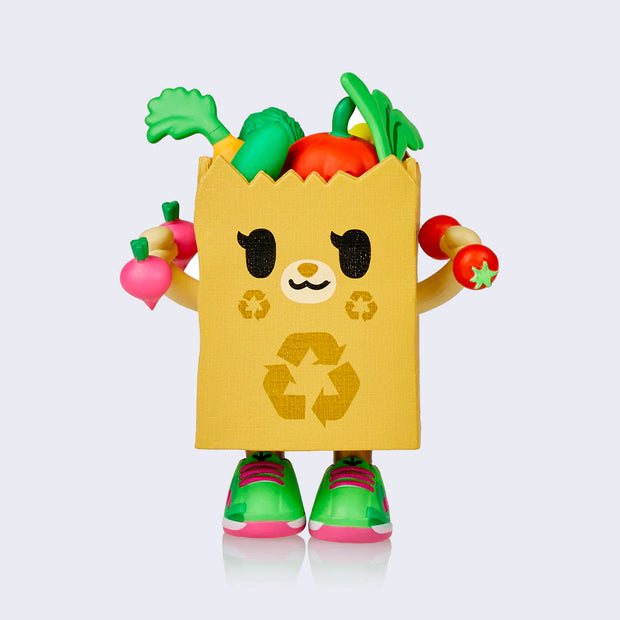 Vinyl figure of a brown kraft grocery bag, with a cartoon animal face and various fruits and veggies popping out of the top. It holds up two dumbbells, one made of radishes and the other made of tomatoes.