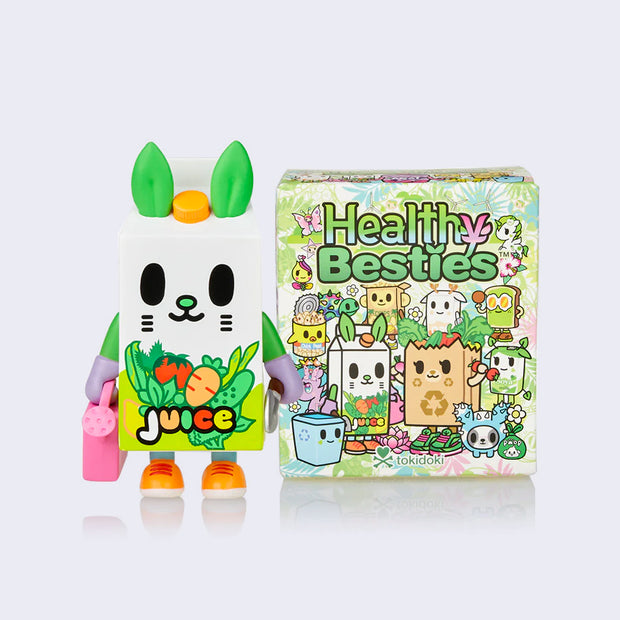 Vinyl figure of a cartoon style juice cartoon, with a smiling animal face. It holds a garden shovel in one hand and a pink watering can in the other. It stands next to its product packaging.