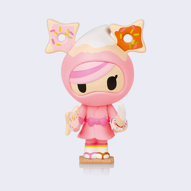 Donutella figure, dressed as a pink ninja with two ninja star shaped sprinkle donuts as ears. She holds a sword that looks like a banana with a pink sprinkle donut hilt, and another ninja star shaped donut in the other hand.