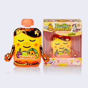 Vinyl figure of a cartoon style apple sauce pack, tropical flavored. It is sunset yellow and orange with gold metallic elements and is in a meditation pose, with a smile on its face. It sits next to its clear product packaging.