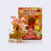 Vinyl semi transparent amber colored unicorn with illustrated peaches on its side. It has a peach colored mane and a branch with cherry blossoms and a shiny peach atop them on its head. Behind is its orange display blind box, featuring illustrations of fruit themed unicorns and imagery.