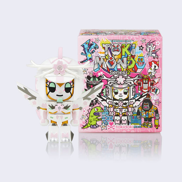 Vinyl figure next to display box. Figure of a mech style character, with helmet, armor and wings, decorated as a sakura tree with light pink cherry blossom accents.