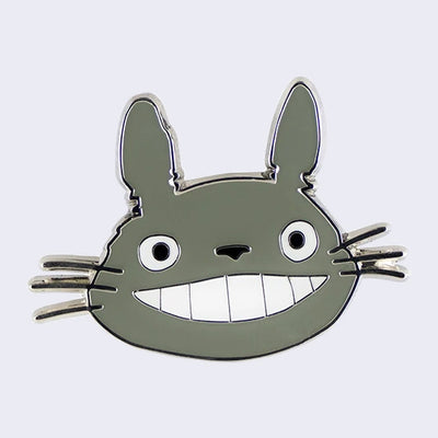 Enamel pin of a close up of Totoro's smiling face, head only.