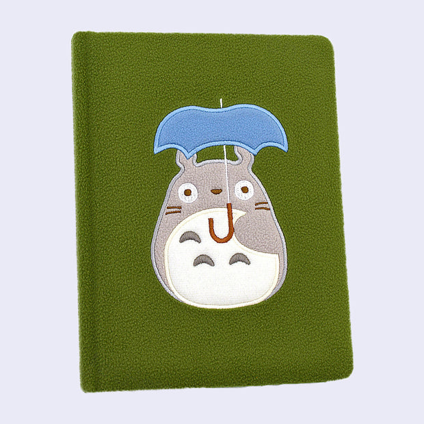 Green plush surface journal, with a simplified embroidery of Totoro holding a blue umbrella.