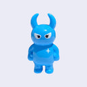 Cyan colored vinyl figure character, standing with arms at its side. It has a round head with curved horns and simple angry eyes with no other facial features. It has a white sparkle on its upper right chest.