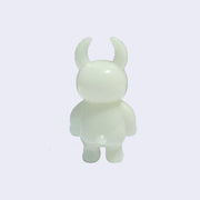 Back view of light yellow/green colored vinyl figure character, standing with arms at its side. It has a round head with curved horns and a small spherical bump for a tail.