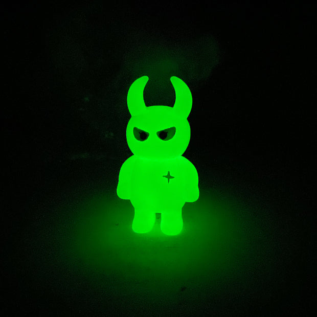 Glow in the dark colored vinyl figure character, standing with arms at its side. It has a round head with curved horns and simple angry eyes with no other facial features. It has a white sparkle on its upper right chest.