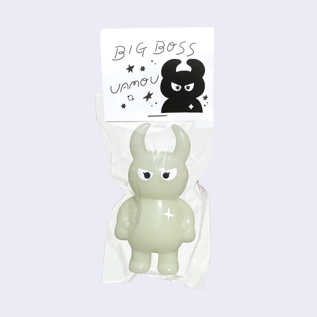 Light yellow/green colored vinyl figure character, standing with arms at its side. It has a round head with curved horns and simple angry eyes with no other facial features. It has a white sparkle on its upper right chest. Character is inside of a plastic bag with a white hang tag that says "Big Boss Uamou" with an illustration of the figure.