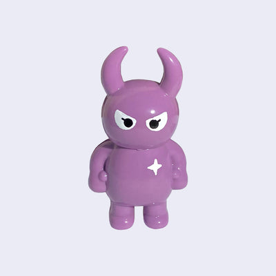 Mauve colored vinyl figure character, standing with arms at its side. It has a round head with curved horns and simple angry eyes with no other facial features. It has a white sparkle on its upper right chest.