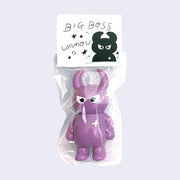 Mauve purple colored vinyl figure character, standing with arms at its side. It has a round head with curved horns and simple angry eyes with no other facial features. It has a white sparkle on its upper right chest. Character is inside of a plastic bag with a white hang tag that says "Big Boss Uamou" with an illustration of the figure.