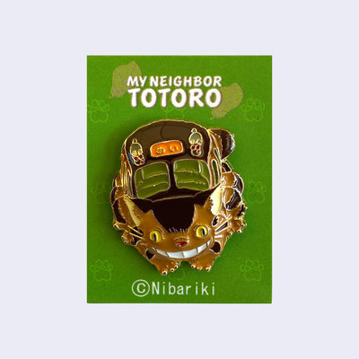 Enamel pin of a smiling Catbus, crouched down as if about to bound up. On a green backing card with "My Neighbor Totoro" written across the top.
