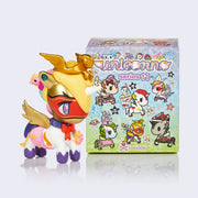 Vinyl unicorno figure next to its display box. Figure is a unicorn dressed as a super hero, with purple, pink and white outfit and red eye mask. It has a golden crown designed as a Pegasus.