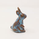 Brown and blue ceramic simplistic shaped bunny, without any distinct facial features. Its ears are up and one paw is raised, curiously.