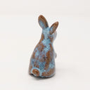 Brown and blue ceramic simplistic shaped bunny, without any distinct facial features. Its ears are up and one paw is raised, curiously.