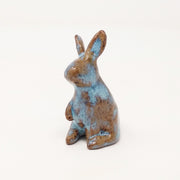 Brown and blue ceramic simplistic shaped bunny, without any distinct facial features. Its ears are up and one paw is raised, curiously.