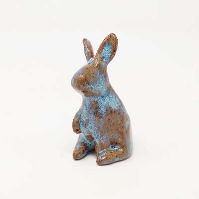 Brown and blue ceramic simplistic shaped bunny, without any distinct facial features. Its ears are up and one paw is raised, curiously.