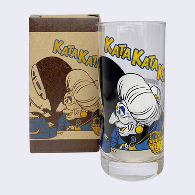 Glass cup with a screen printed design on the outside, imagery from Spirited Away of an old lady with large hair and jewelry, seweing next to No Face, both looking happy. "Kata Kata Kata" is written in yellow font along the top.