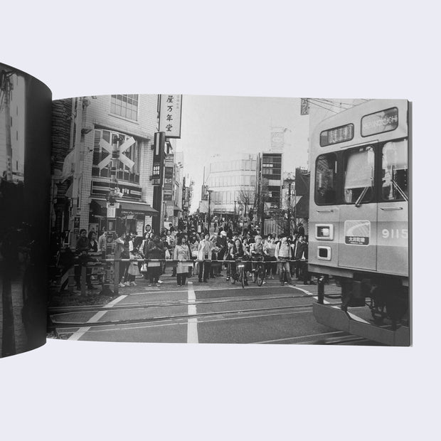 Open zine page with a full bleed black and white photo of a busy Japanese street scene, with people waiting for a train car to pass.
