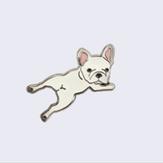 Gif of enamel pin of a cream colored French Bulldog, laying on its stomach and its head turned to look straight at the viewer. One image is of pin in light, the other is of pin glowing in the dark.
