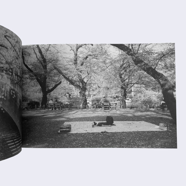 Open zine page with a full bleed black and white photo of a person laying on a large blanket in the middle of a tree covered park.