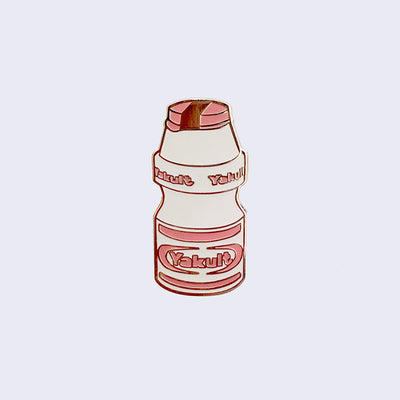 Enamel pin of a small Yakult bottle packaging, white with red design accents.
