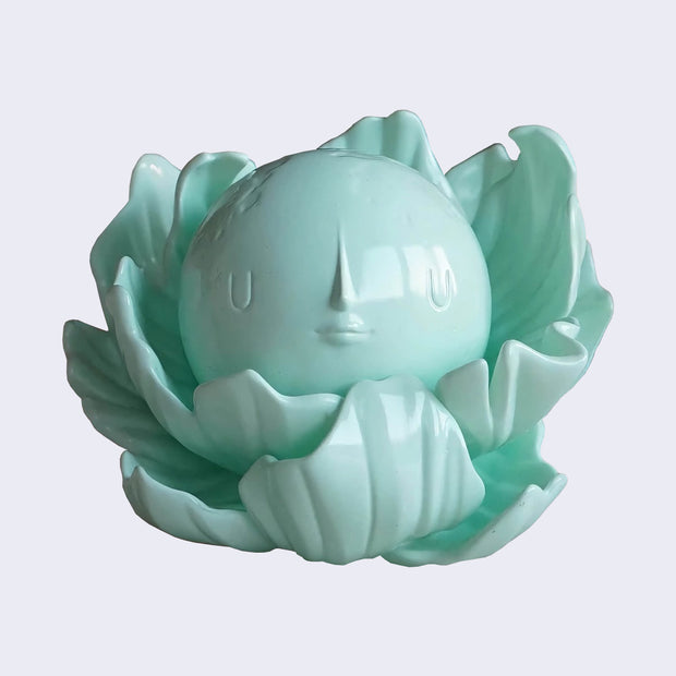 Moonflower picture of a turquoise colored vinyl toy of a moon with a face inside of flower petals, as if it's a plant! 